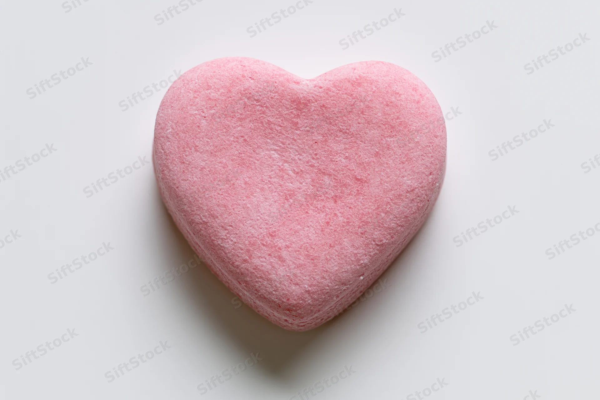 Pink heart-shaped candy lying flat on white surface