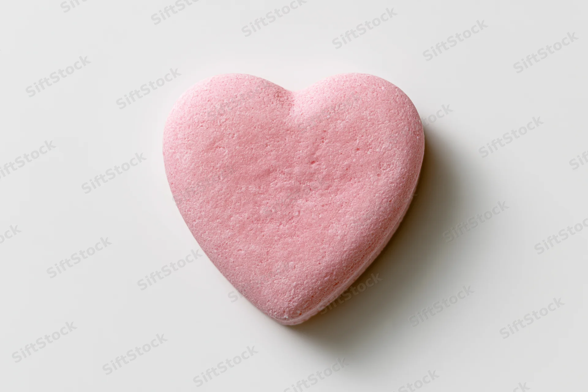 Pink heart-shaped candy lying flat on white surface