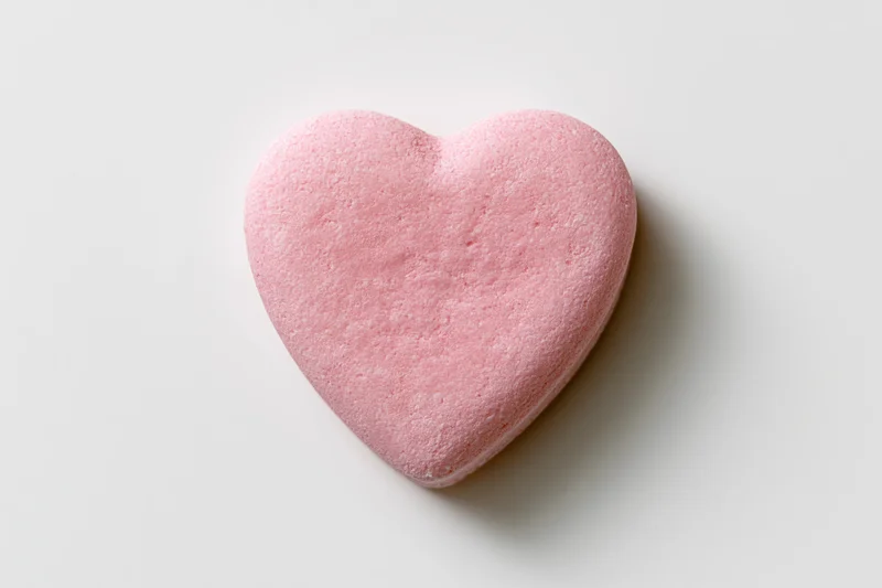 Pink heart-shaped candy lying flat on white surface