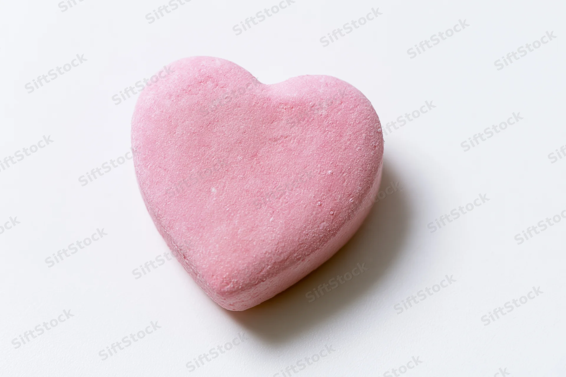 Pink heart-shaped candy lying on white surface