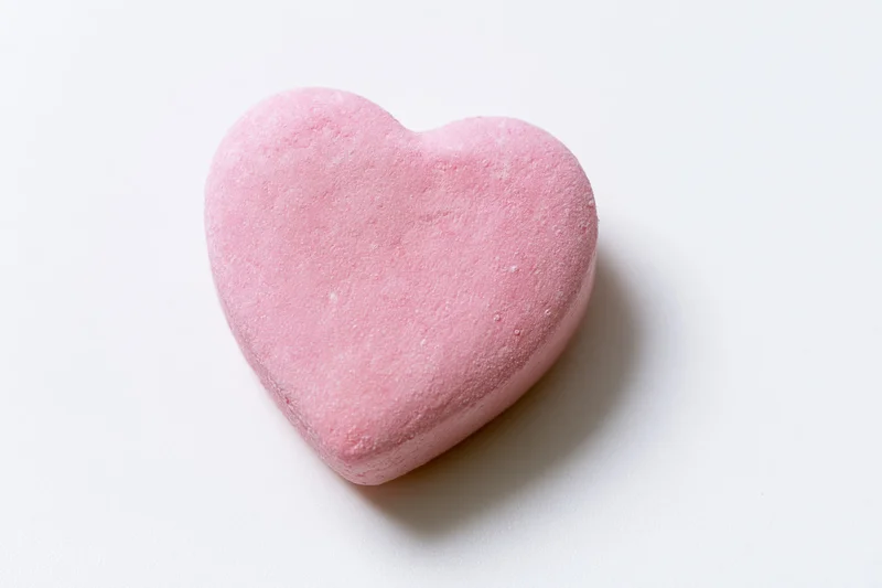 Pink heart-shaped candy lying on white surface
