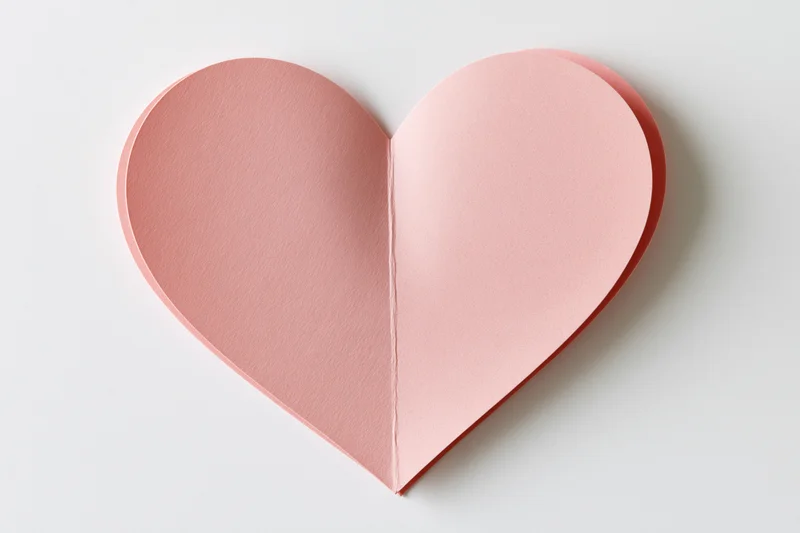 Pink paper heart cutout lying flat on white surface
