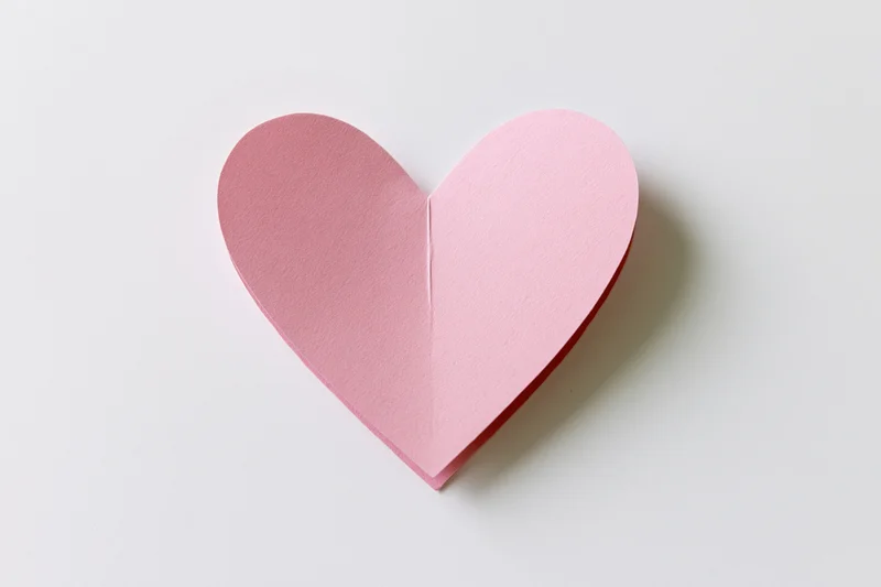 Pink paper heart cutout on white background with copyspace