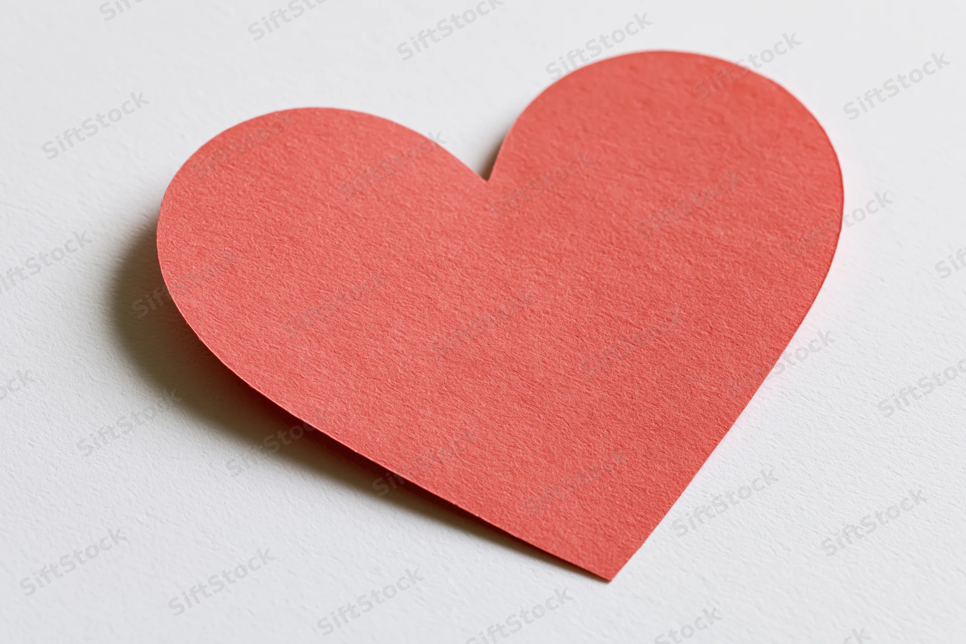 Red paper heart cutout lying flat on white surface