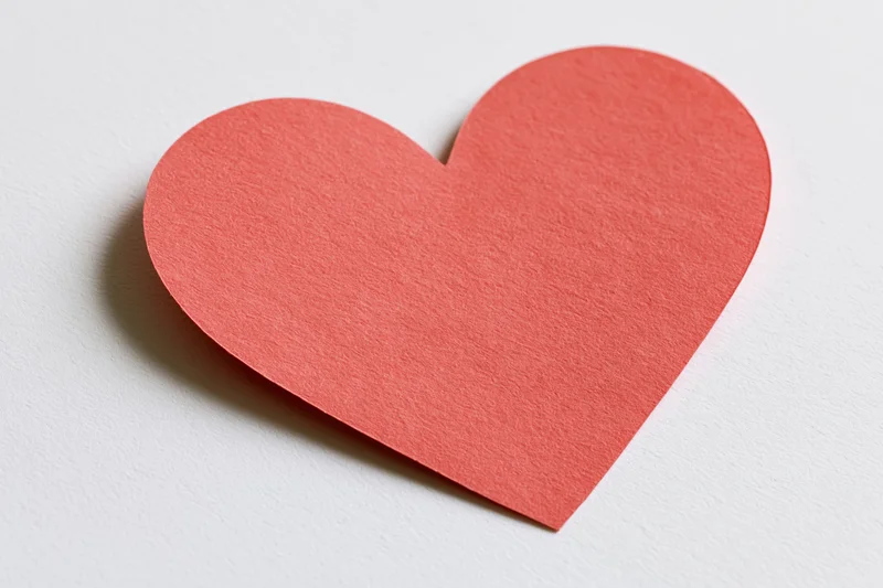Red paper heart cutout lying flat on white surface