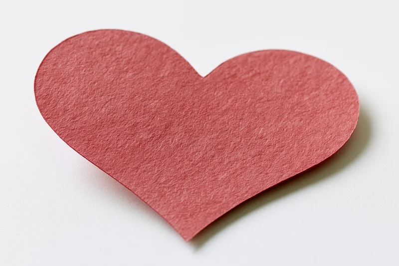Red paper heart cutout lying flat on white surface