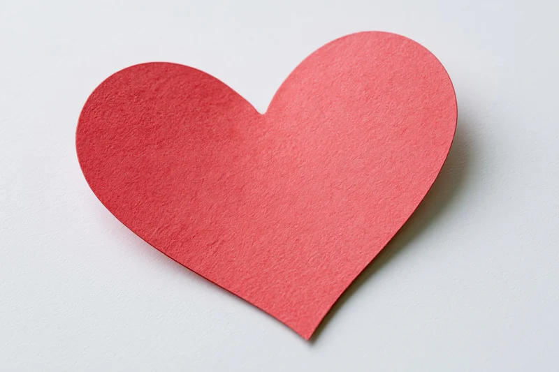 Red-pink paper heart cutout lying flat on white surface