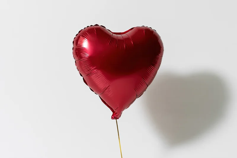 Red foil heart-shaped balloon floating on gold string against white background