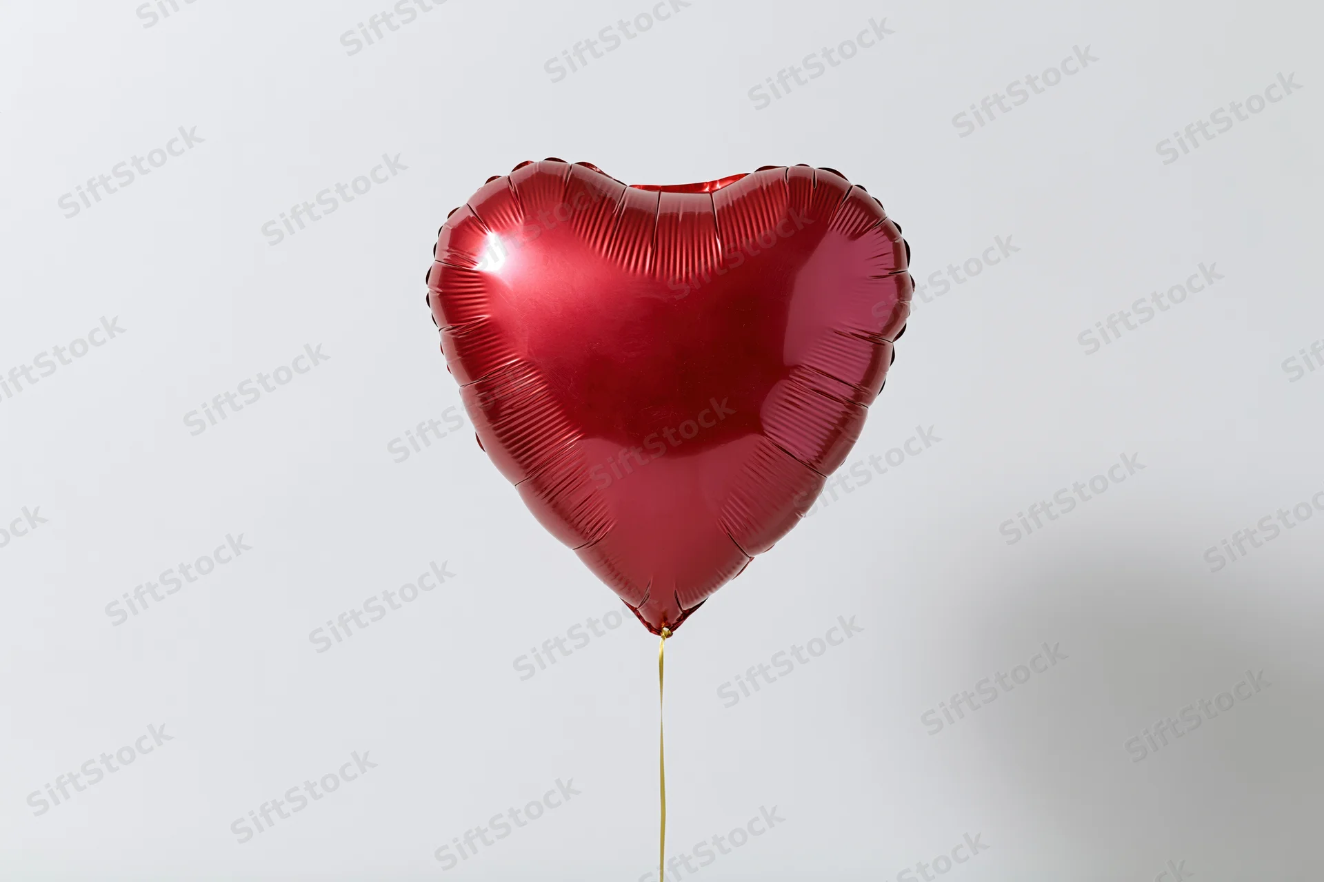Red foil heart-shaped balloon floating on a thin gold string against a plain white background