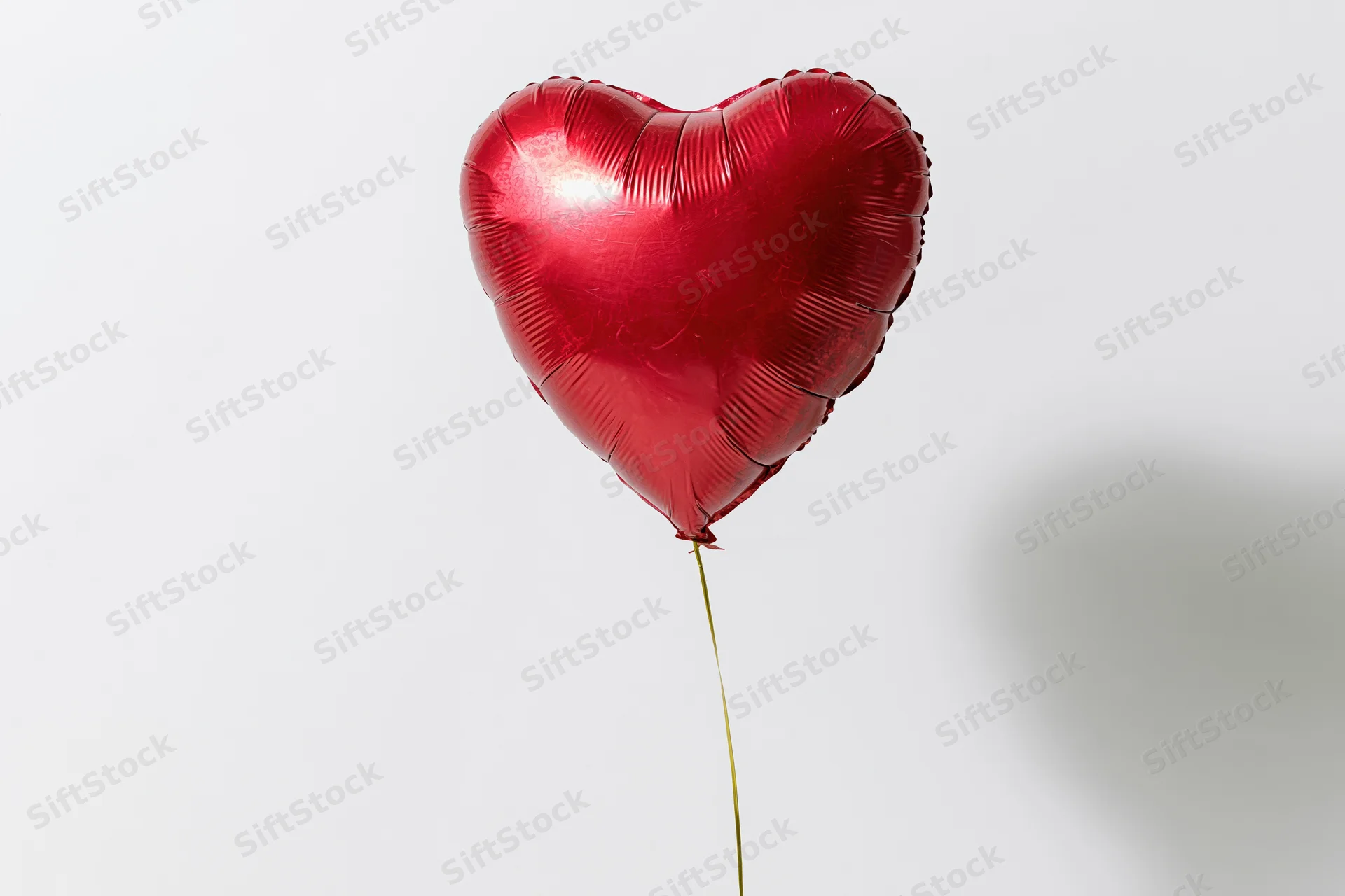 Red foil heart-shaped balloon floating on a gold string against white background