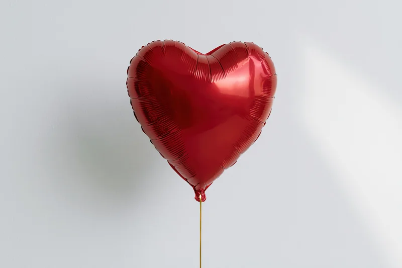 Red foil heart-shaped balloon floating on a gold string against a white background