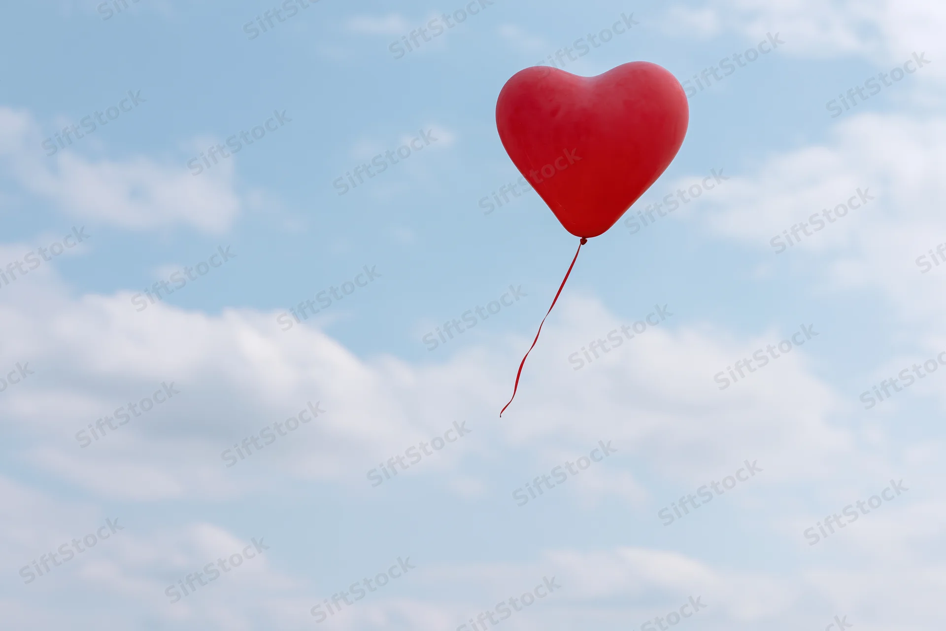 Red heart-shaped balloon floating in a blue sky with scattered clouds