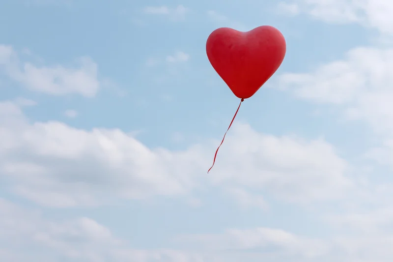 Red heart-shaped balloon floating in a blue sky with scattered clouds