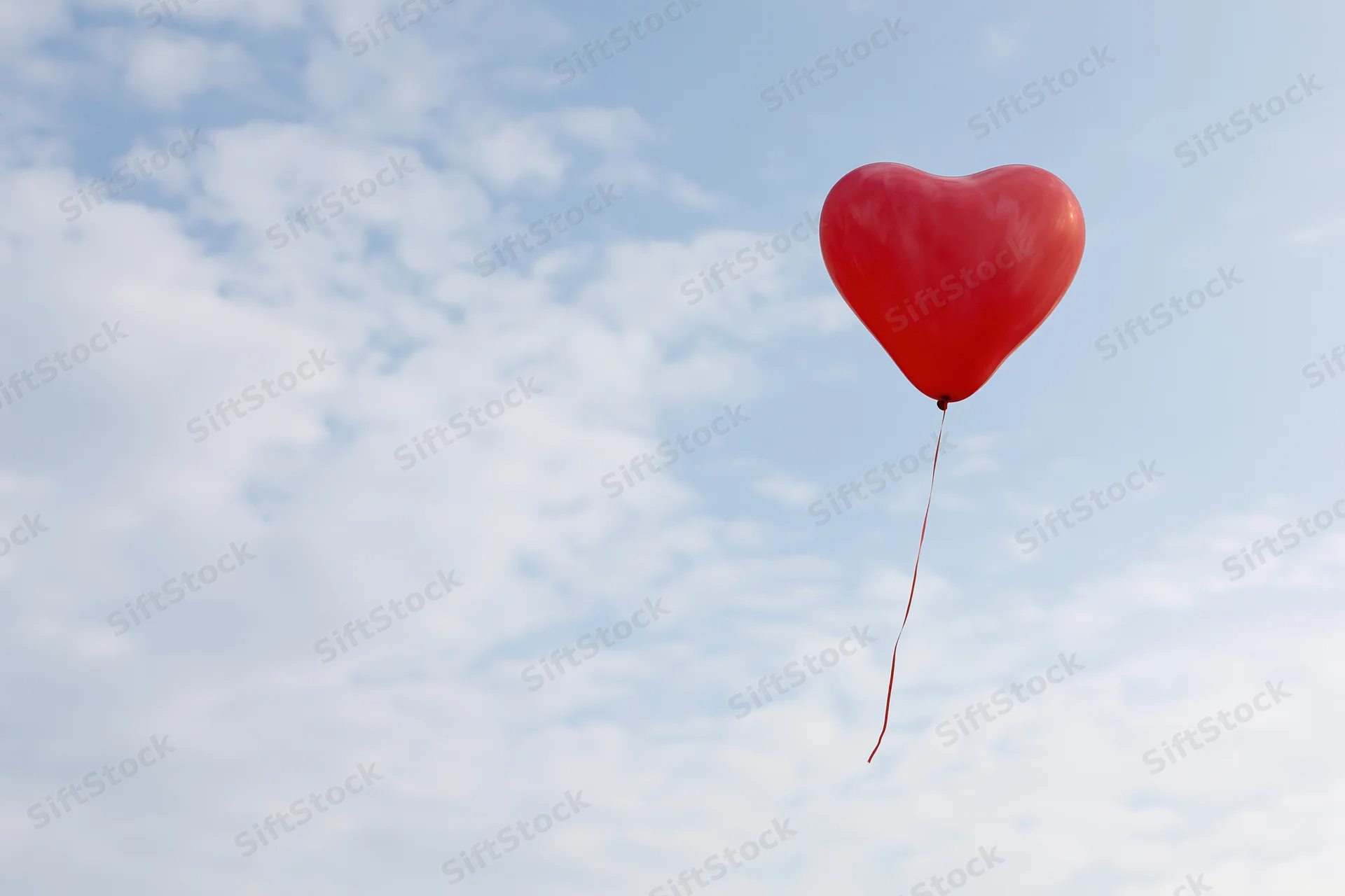 Red heart-shaped balloon floating in a cloudy sky