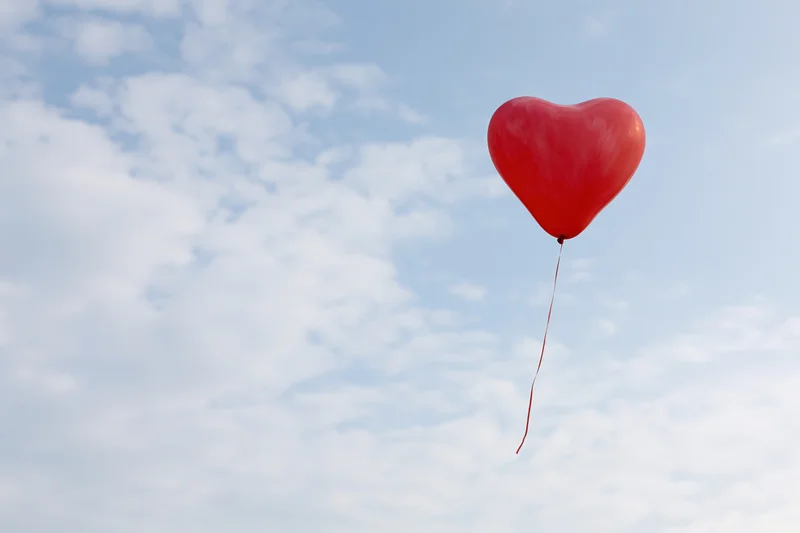 Single red heart-shaped balloon floating freely against blue sky