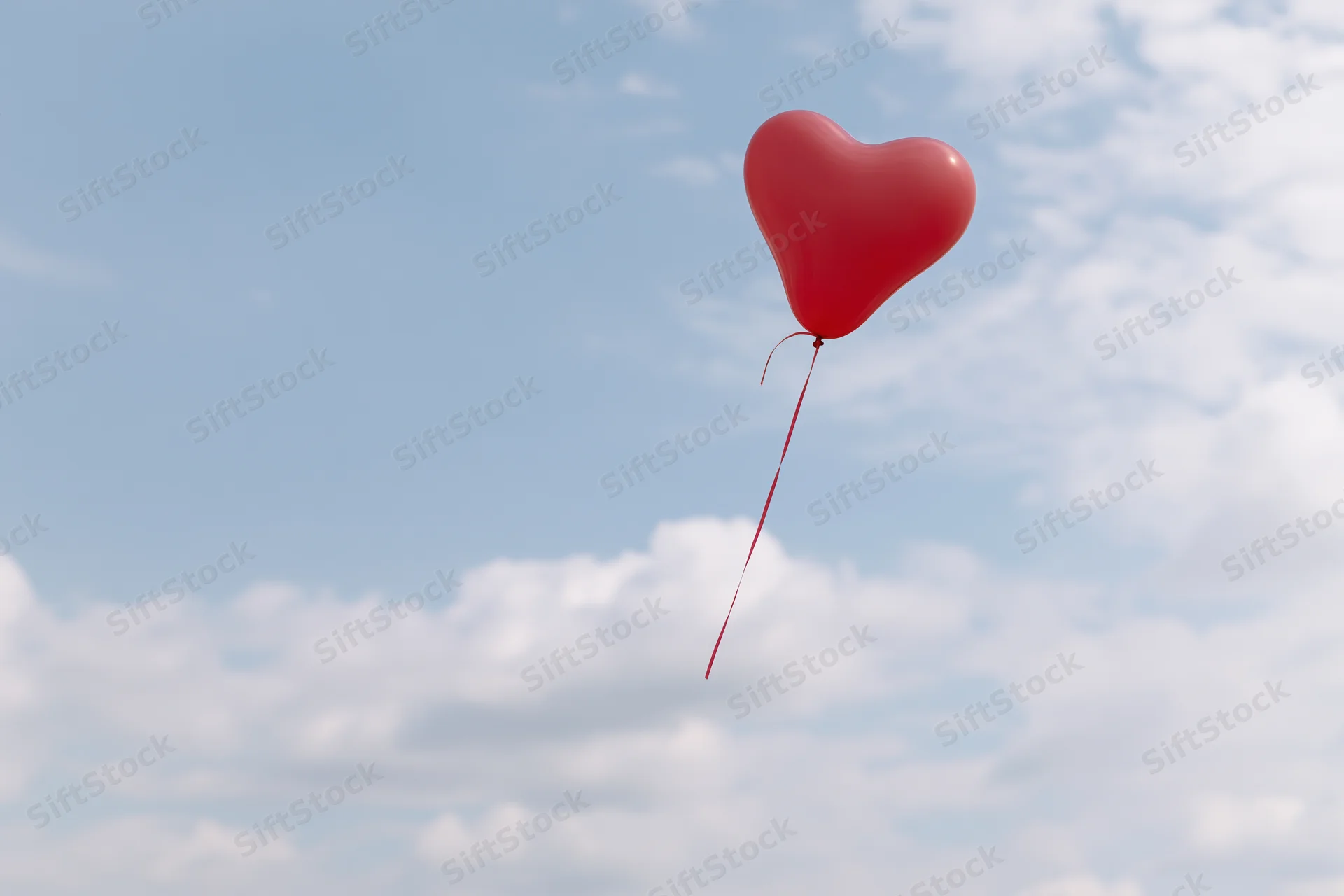 Red heart-shaped balloon floating in a partly cloudy sky
