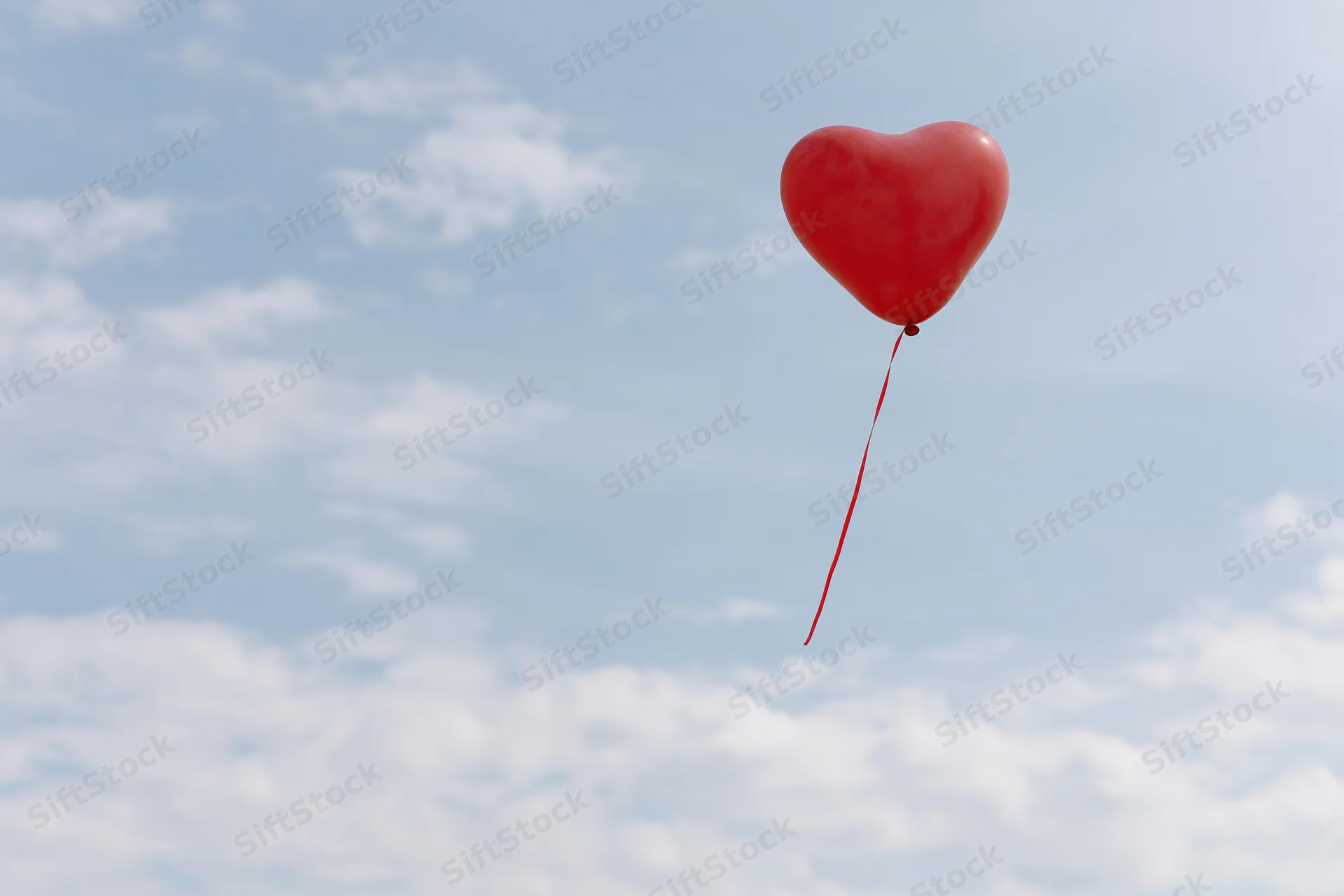 Red heart-shaped balloon floating in a cloudy sky