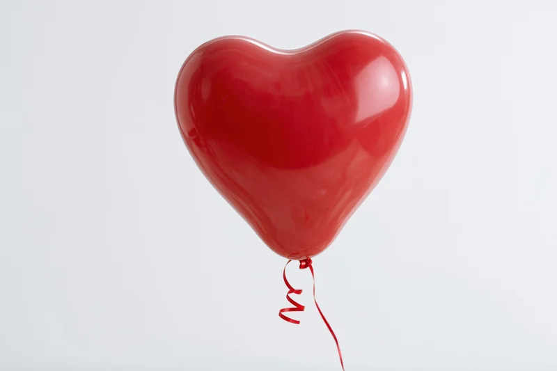 Red heart-shaped balloon floating against white background with ribbon trailing below