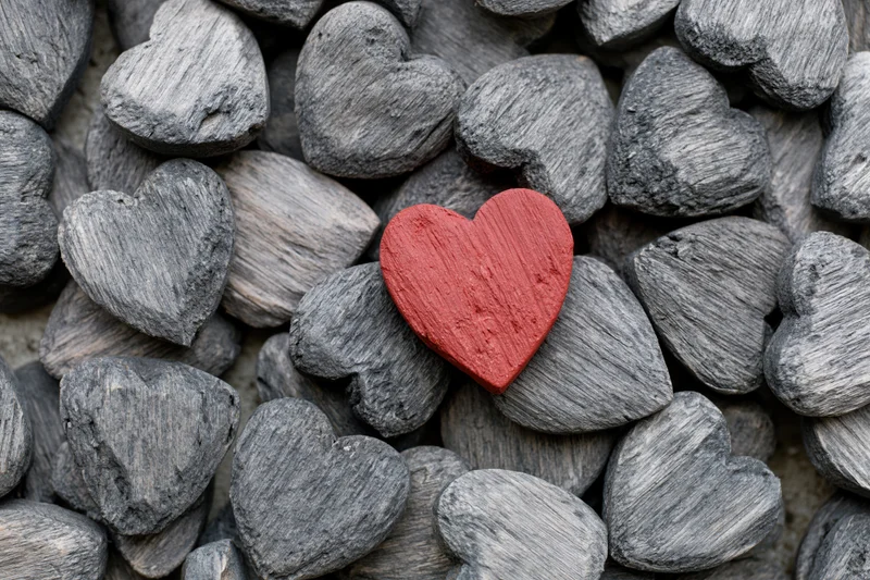 Red painted wooden heart resting among gray weathered stone hearts in a pile