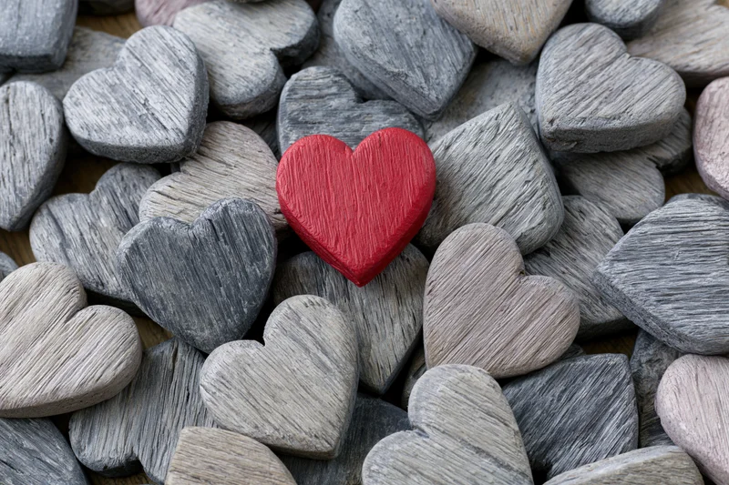 Red painted wooden heart resting among gray stone hearts in a pile