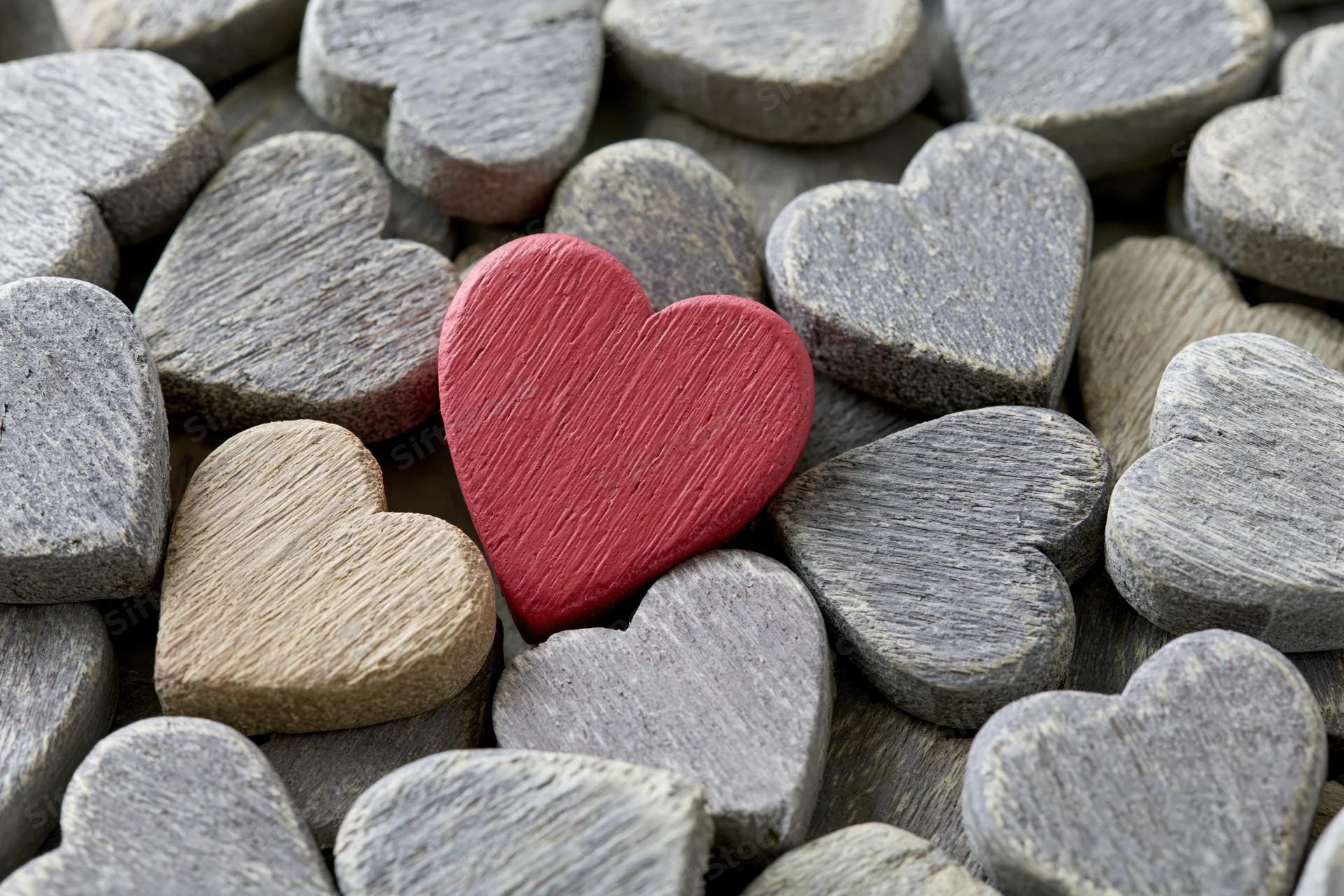 Red painted wooden heart resting among gray stone hearts in a pile