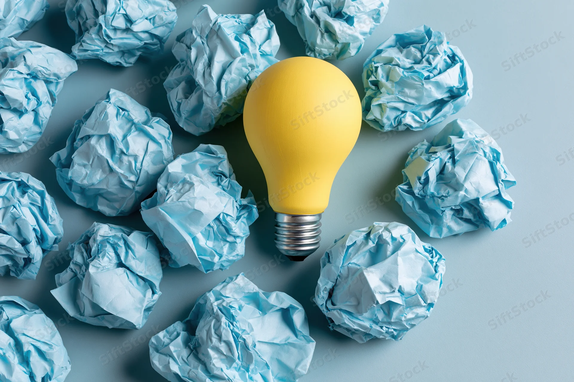 Yellow lightbulb surrounded by crumpled blue paper on a flat surface