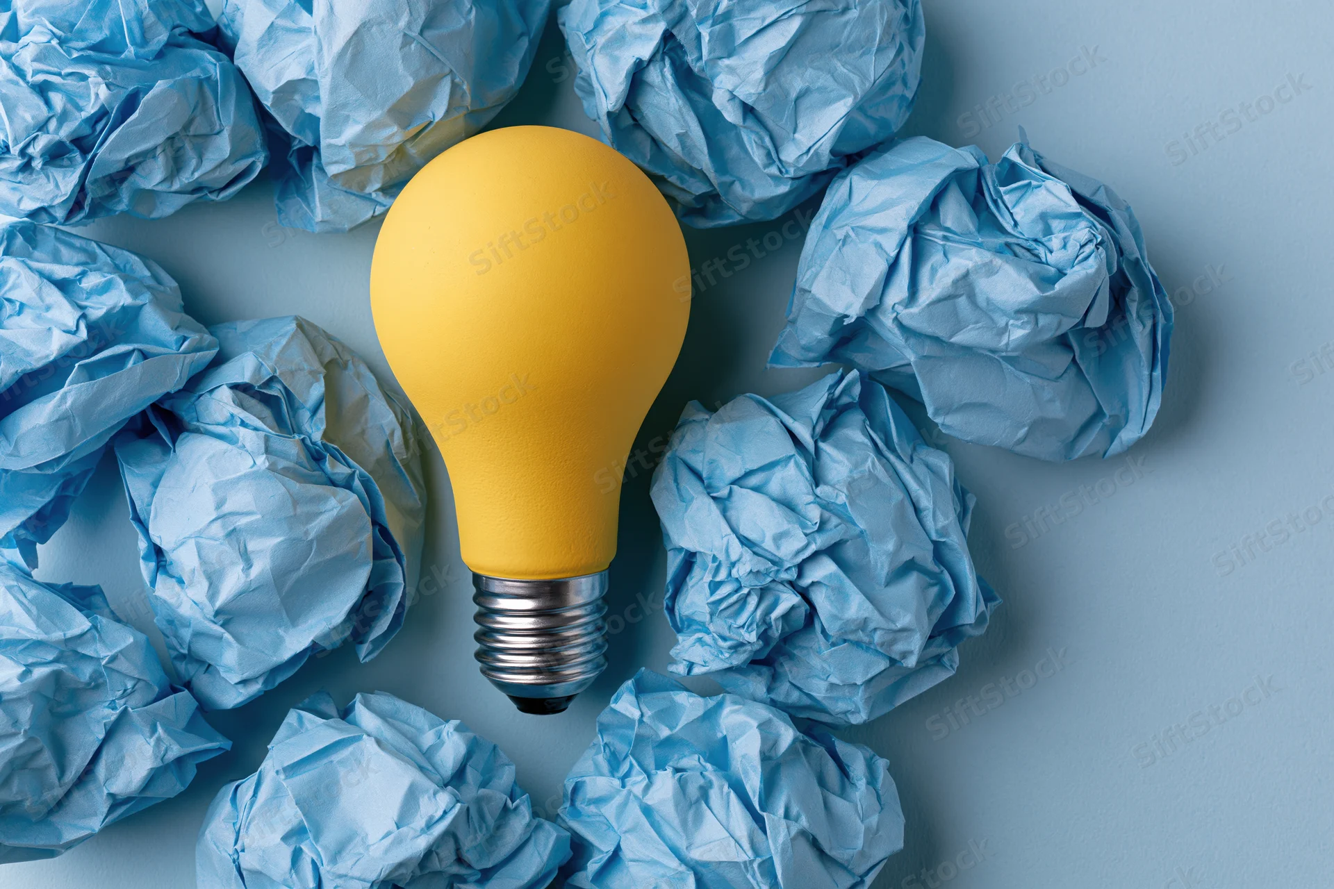 Yellow lightbulb surrounded by crumpled blue paper on a flat surface