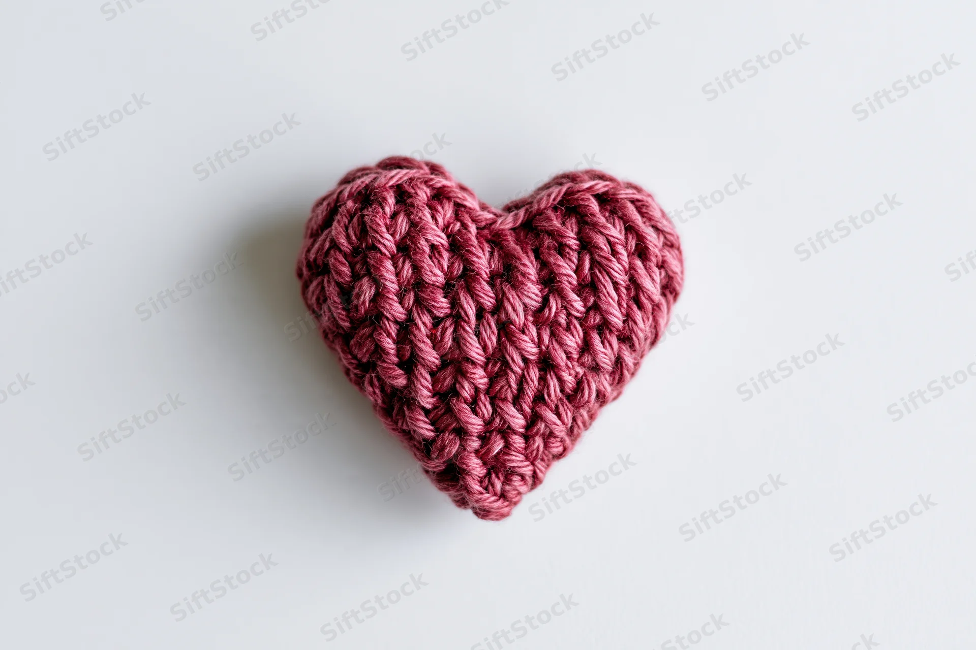 Crocheted heart made of crimson pink yarn resting centered on white surface