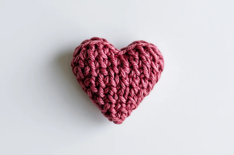 Crocheted heart made of crimson pink yarn resting centered on white surface