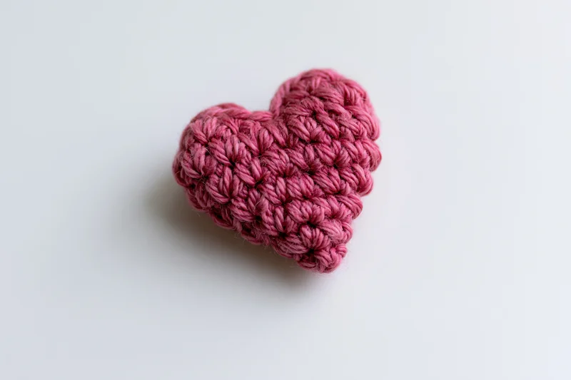 Crocheted pink yarn heart resting on white surface