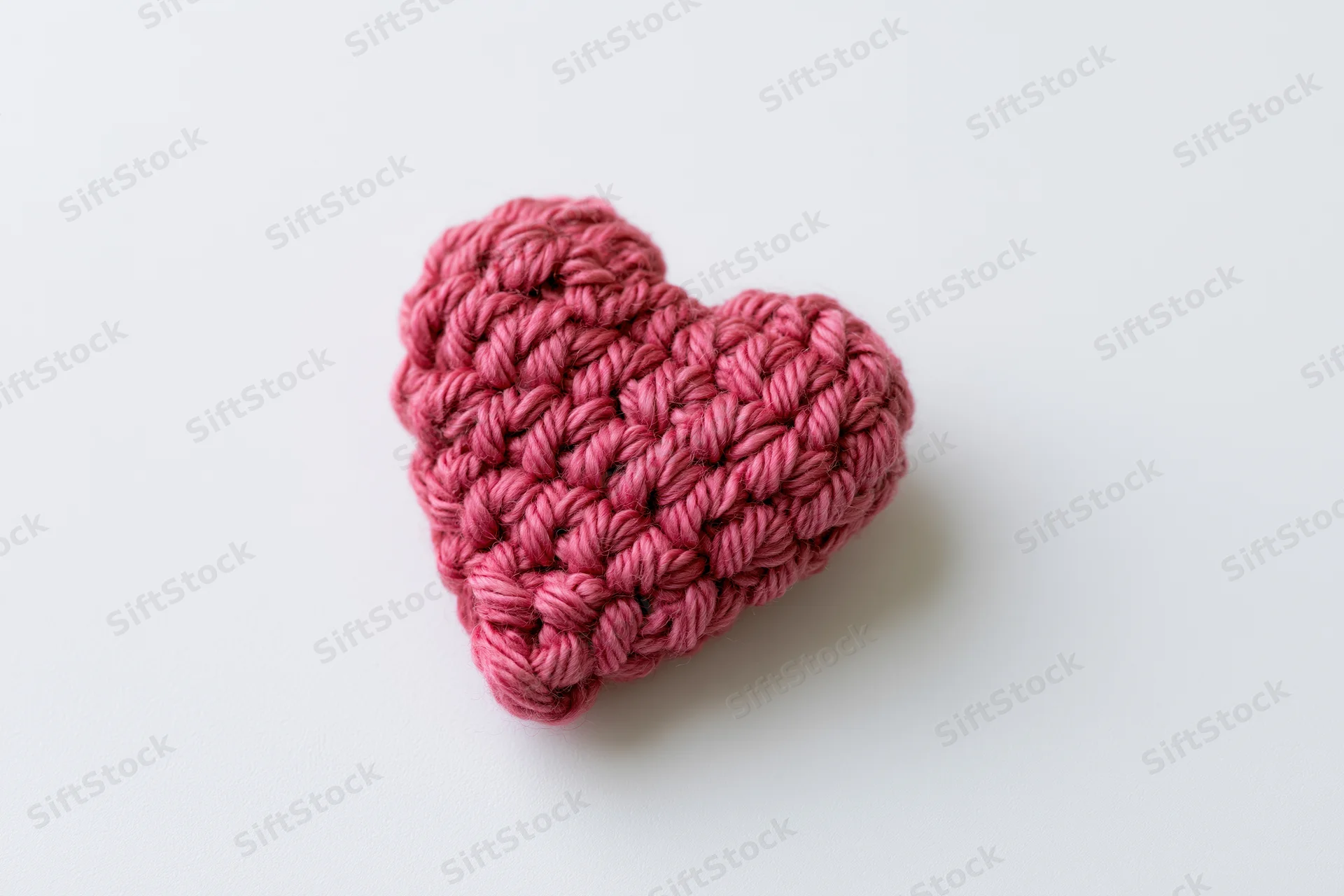 Crocheted pink yarn heart resting on white surface