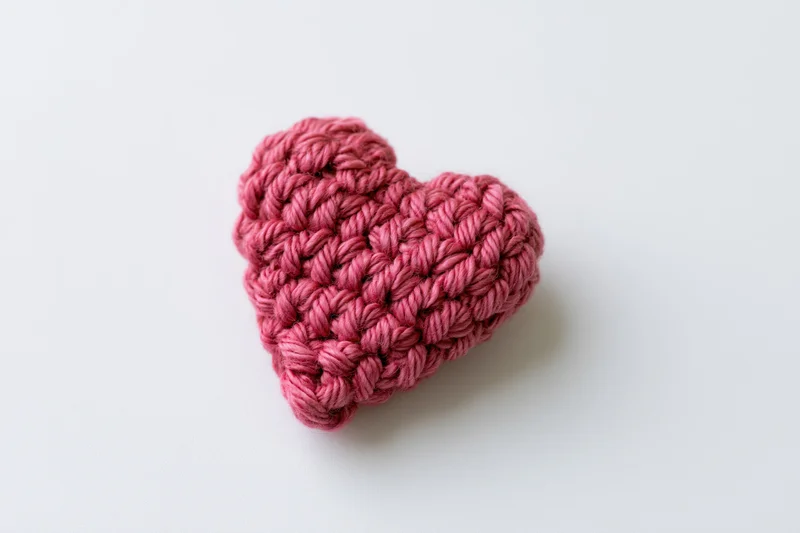 Crocheted pink yarn heart resting on white surface