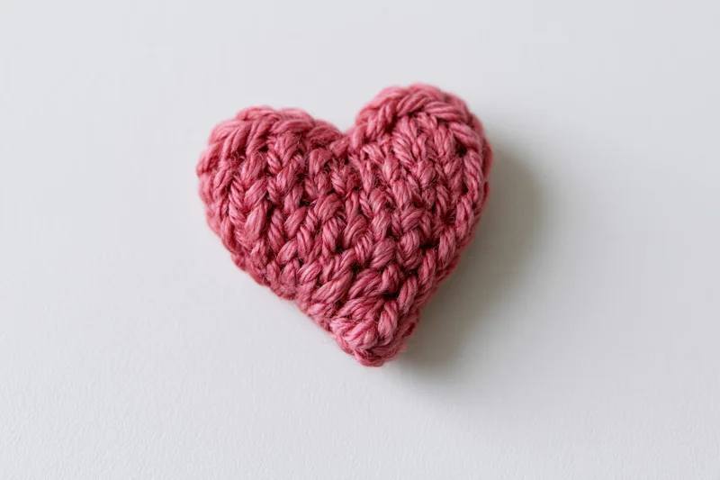 Crocheted pink yarn heart resting on white surface