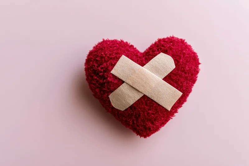 Red fluffy heart with beige bandages in cross shape on pink surface
