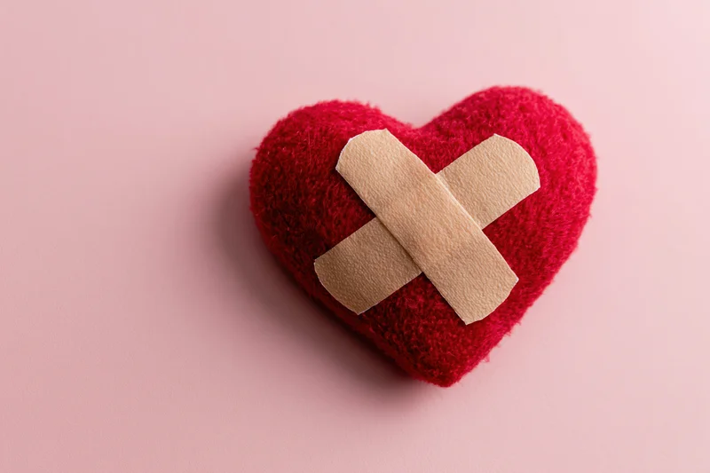 Red plush heart with beige bandages in cross shape on pink background