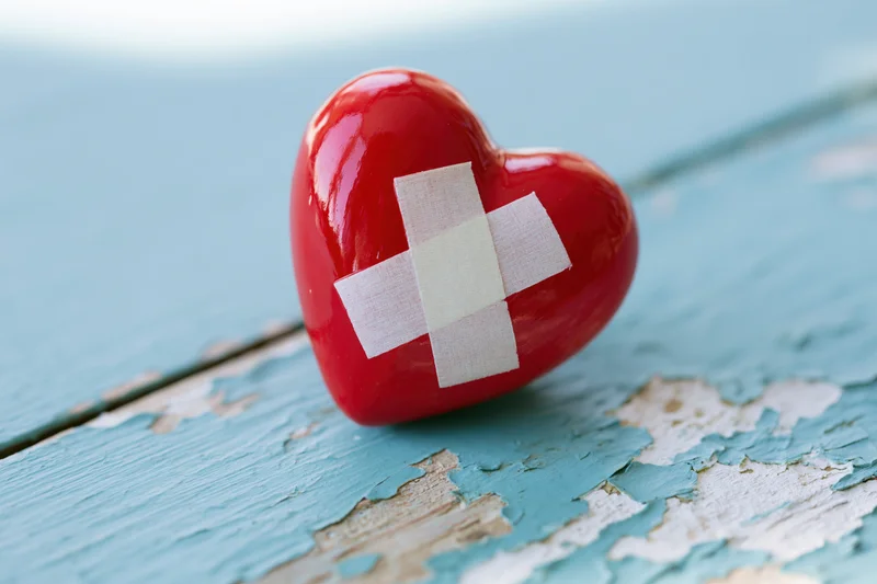 Red glossy ceramic heart with white bandage cross on weathered blue wooden surface