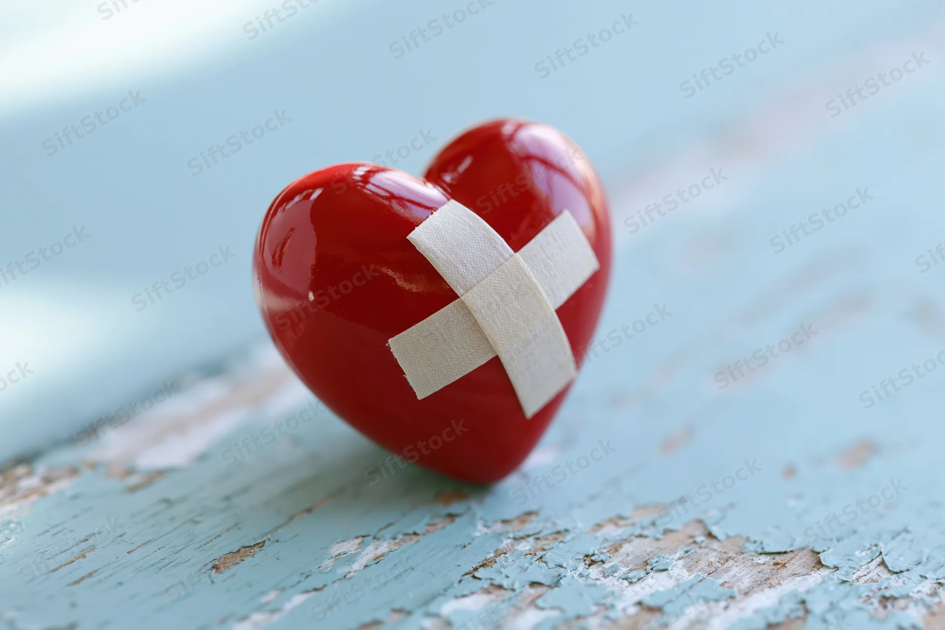Glossy red ceramic heart with white bandage cross on distressed blue wooden surface