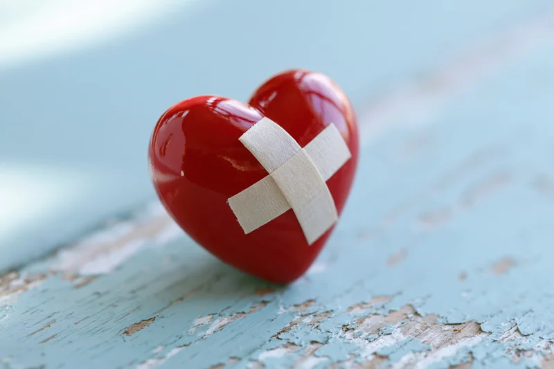 Glossy red ceramic heart with white bandage cross on distressed blue wooden surface