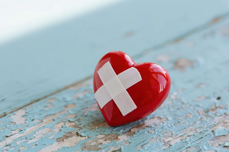 Glossy red ceramic heart with white bandage cross on peeling blue wooden surface