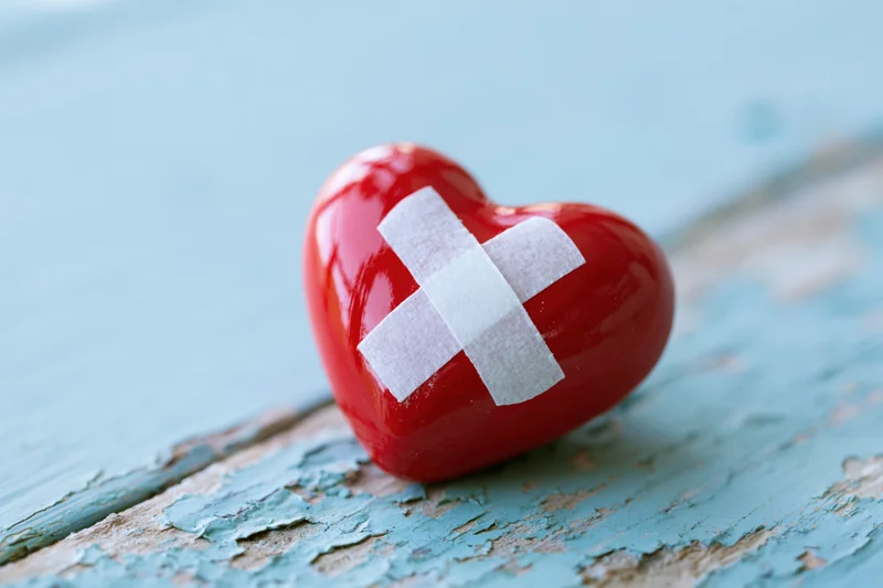 Glossy red ceramic heart with white bandage cross on peeling blue wooden surface