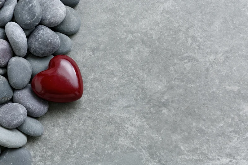 Glossy red ceramic heart among gray pebbles on concrete surface