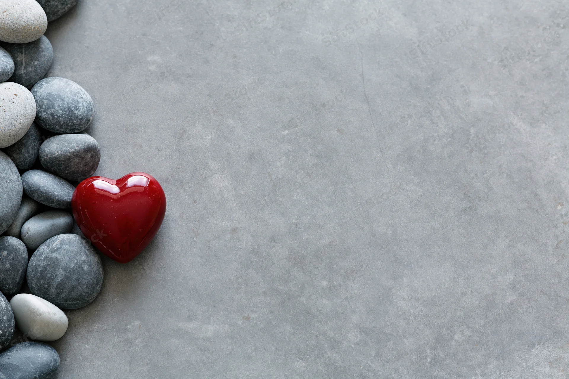 Glossy red ceramic heart among smooth gray pebbles on concrete surface