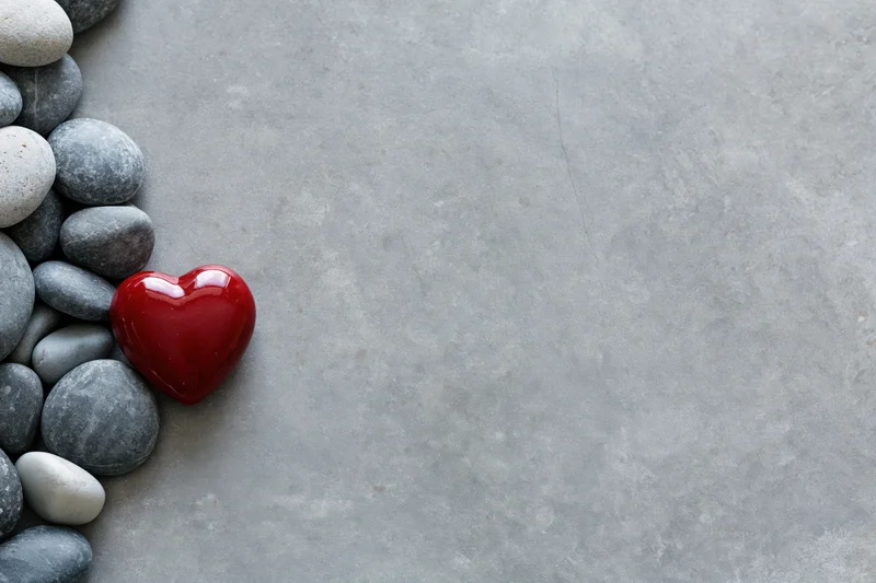 Glossy red ceramic heart among smooth gray pebbles on concrete surface