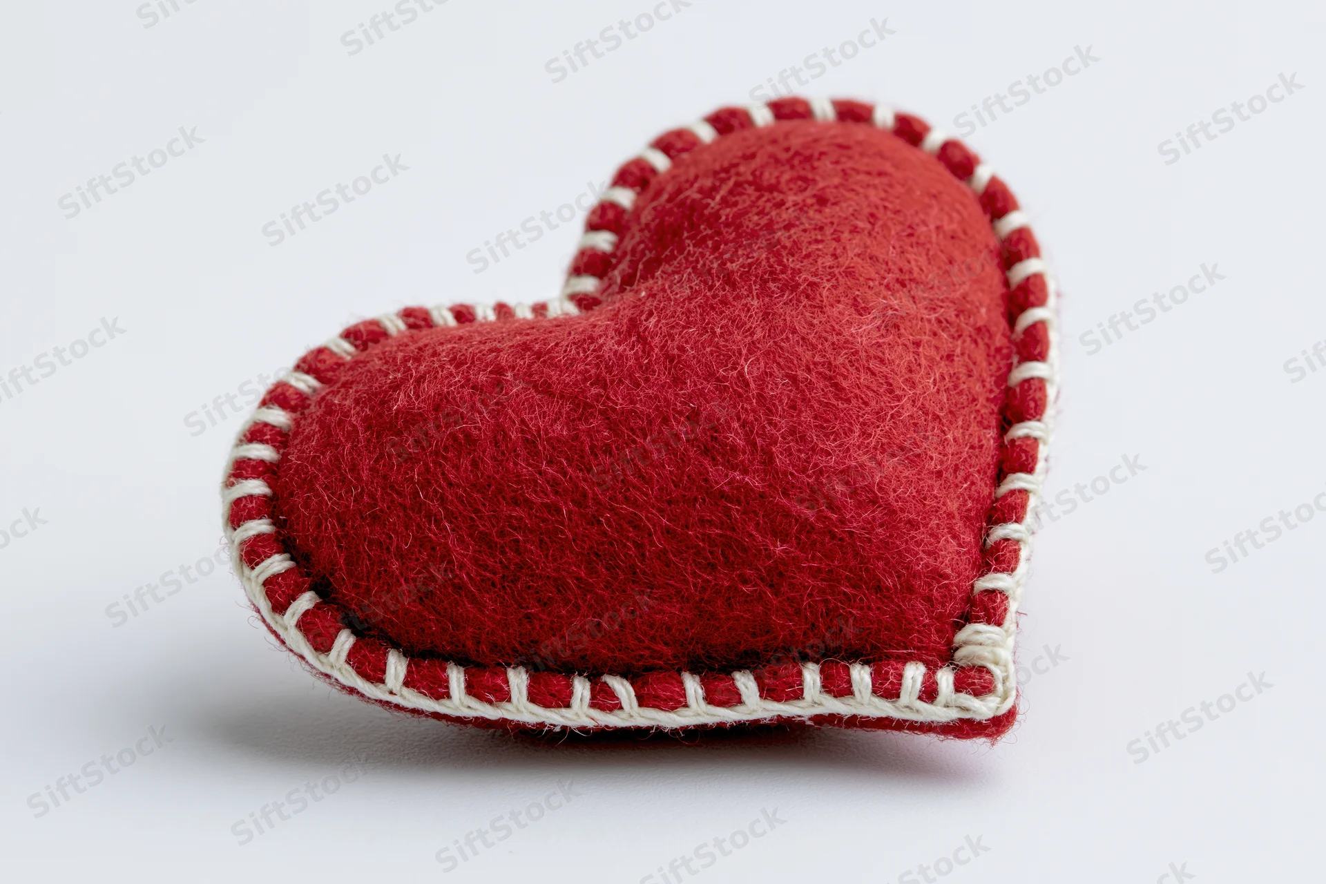 Red felt heart pillow with white blanket stitch on white background