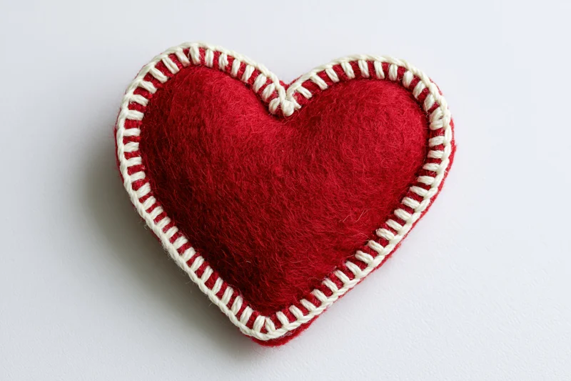 Handmade red felt heart with white blanket stitch on white background
