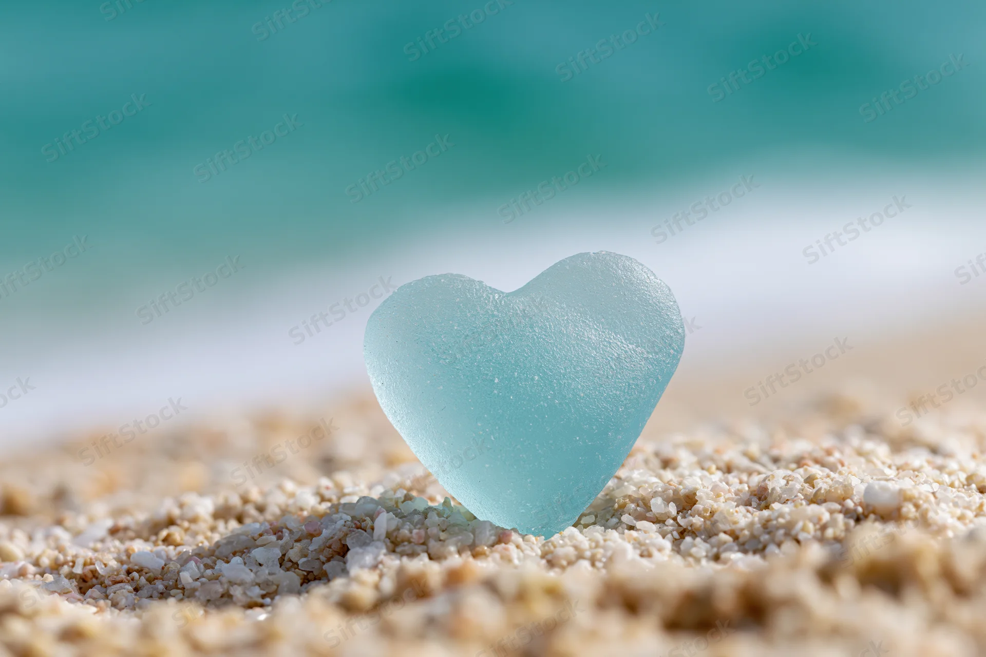 Heart-shaped sea glass resting on sandy beach near ocean waves