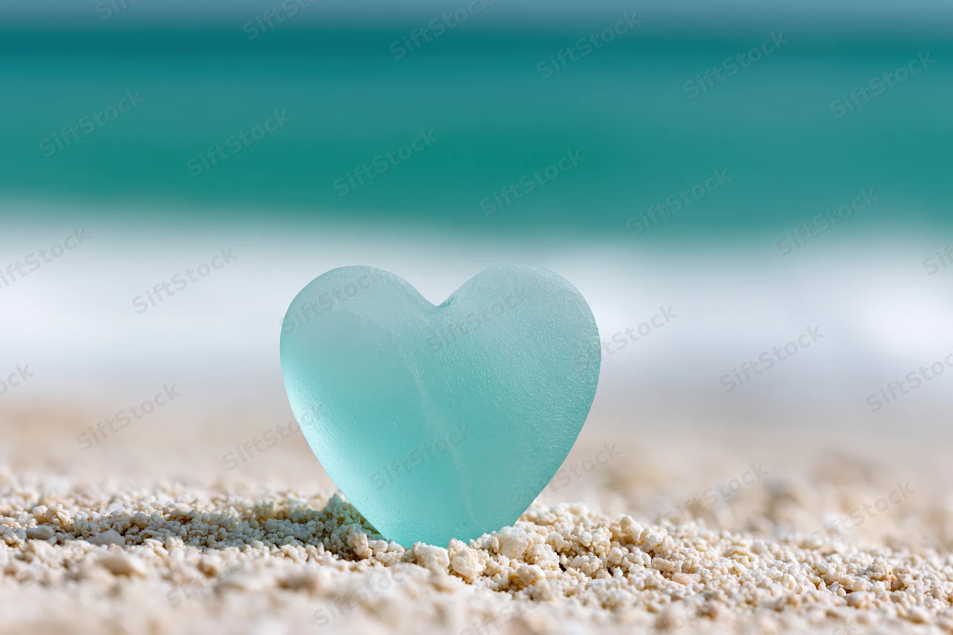 Heart-shaped sea glass resting on sandy beach with ocean in background
