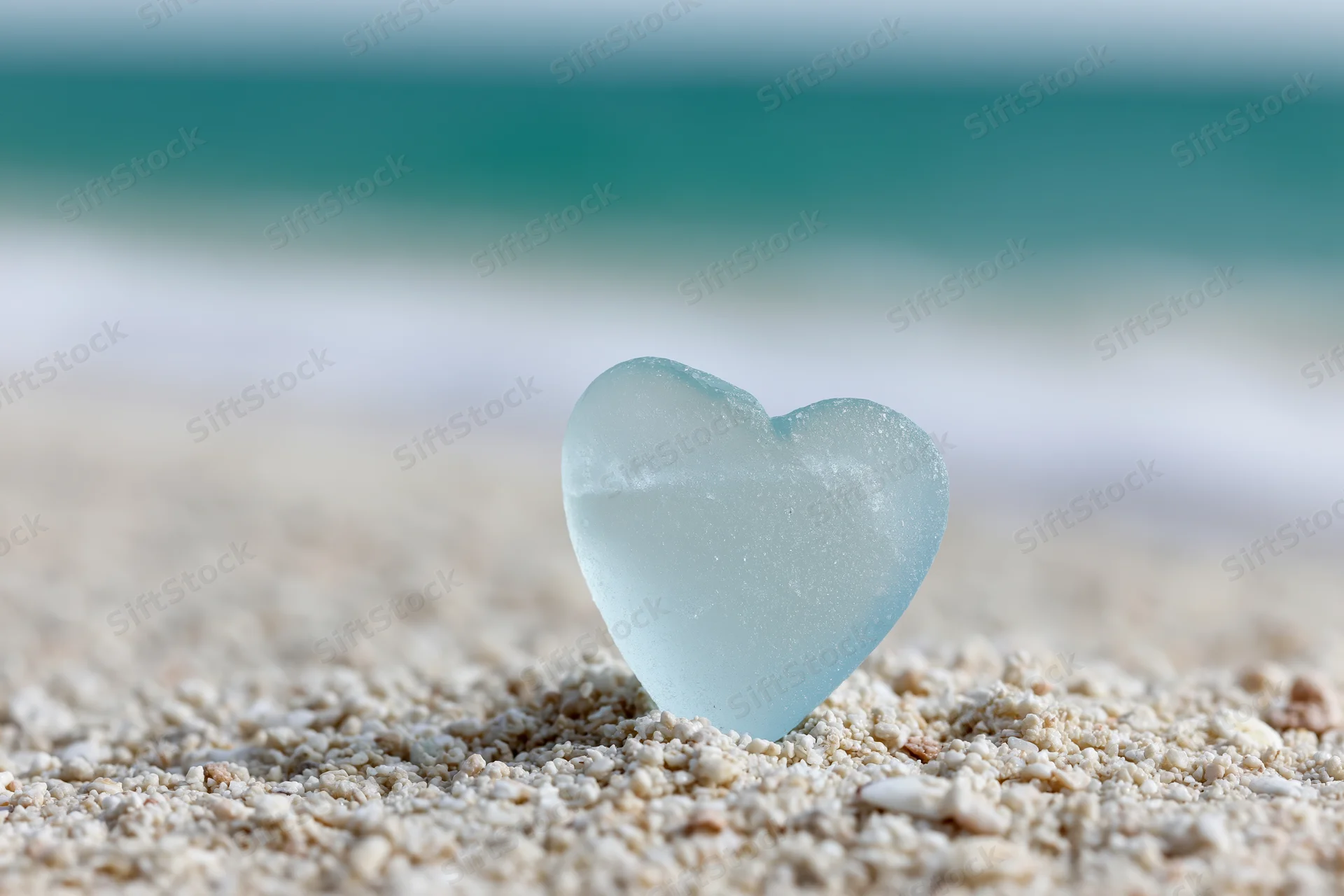 Heart-shaped sea glass resting on sandy beach with ocean in background