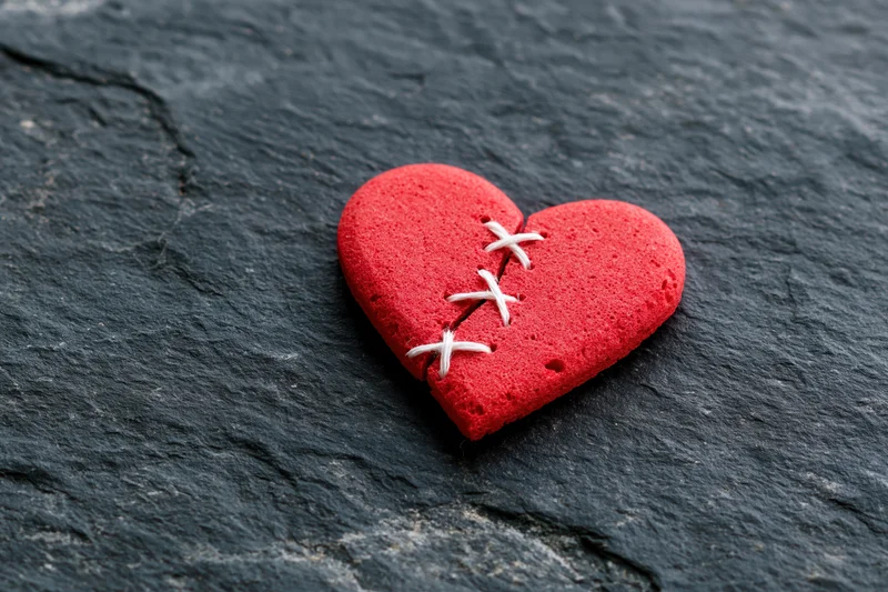 Red foam heart stitched back together on dark slate surface