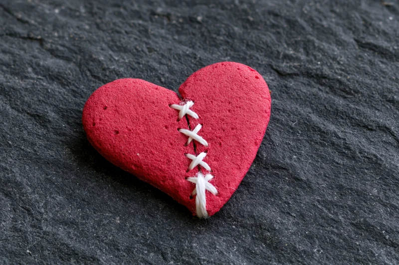 Red foam heart stitched back together on dark stone surface